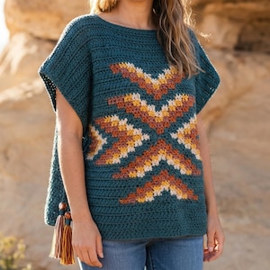 May include: A teal crochet top featuring a geometric pattern in shades of orange, yellow, and cream. The garment has short sleeves, a wide neckline, and a side tassel detail with wooden beads. The crochet stitch is horizontal throughout the body.