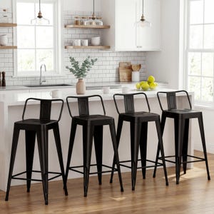 May include: Four black metal bar stools with backs are arranged in front of a white kitchen island. The stools have a minimalist design with a rectangular backrest and a footrest. The kitchen has white subway tile and wooden shelves.