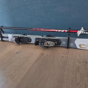 May include: A pair of white and grey skis with black bindings and a pair of black, red, and white ski poles. The skis are labelled "C9" and "150". The ski poles are labelled "LEKI".