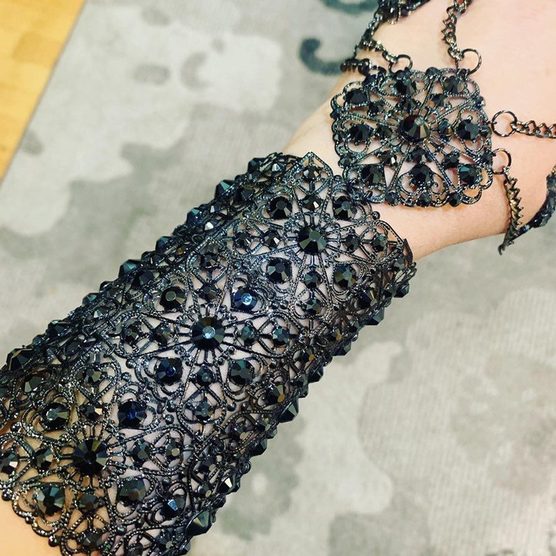 May include: A black lace bracelet with black rhinestones. The bracelet is made of metal and has a delicate design.