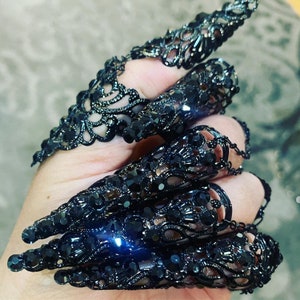 May include: Black lace fingertip rings with a claw-like design. The rings are made of metal and have a black finish.