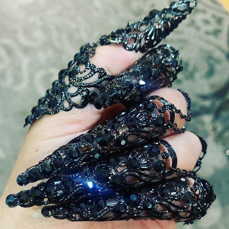 May include: Black lace fingertip rings with a claw-like design. The rings are made of metal and have a black finish.