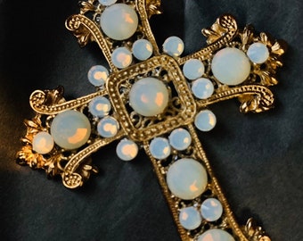 May include: A gold-toned cross pendant with a detailed design and white opal stones.