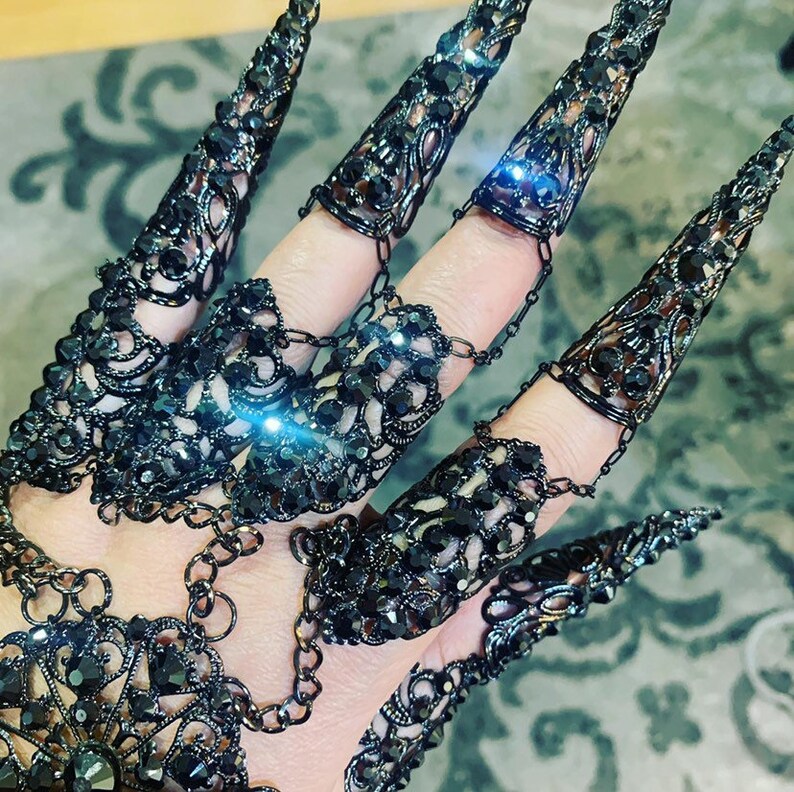 May include: A set of black metal claw rings with rhinestones. The rings are connected by chains and can be worn on multiple fingers.