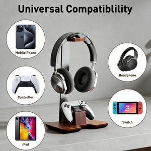 Op de afbeelding: Een houten hoofdtelefoonstandaard met een zwart-zilveren headset en een wit-zwarte controller. De standaard biedt ook plaats aan een mobiele telefoon, iPad en een Switch. De tekst "Universal Compatibility" staat bovenaan.