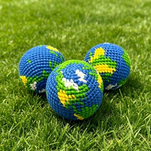 Puede incluir: Tres bolas esféricas de ganchillo con un patrón de globo terráqueo detallado. Cada bola está elaborada con hilo azul para los océanos, hilo verde para las masas terrestres e hilo amarillo y blanco para detalles geográficos en la superficie.