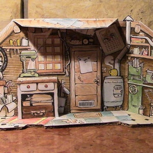 May include: A cardboard model of a workshop featuring a wood-burning stove, a workbench with drawers, a metal fan, a green mixer, and a lathe. The workshop has a window, a door, and a shelf with tools and supplies.