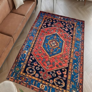 May include: A rectangular area rug with a central red medallion and a blue border. The rug features intricate geometric patterns in shades of red, blue, and gold. The rug is placed on a hardwood floor, and is a decorative element for a living room.