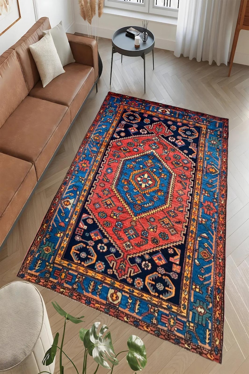 May include: A rectangular area rug with a central red medallion and a blue border. The rug features intricate geometric patterns in shades of red, blue, and gold. The rug is placed on a hardwood floor, and is a decorative element for a living room.