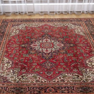 May include: A large, rectangular red oriental rug with an intricate central medallion design. The rug features a detailed border with floral and geometric patterns in shades of red, cream, and navy blue. It is placed on a hardwood floor.