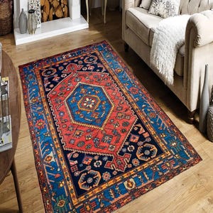 May include: A rectangular area rug with a central geometric design in red, blue, and navy. The rug features a detailed border with repeating patterns and is placed on a hardwood floor. The rug's design includes a central medallion and corner elements.