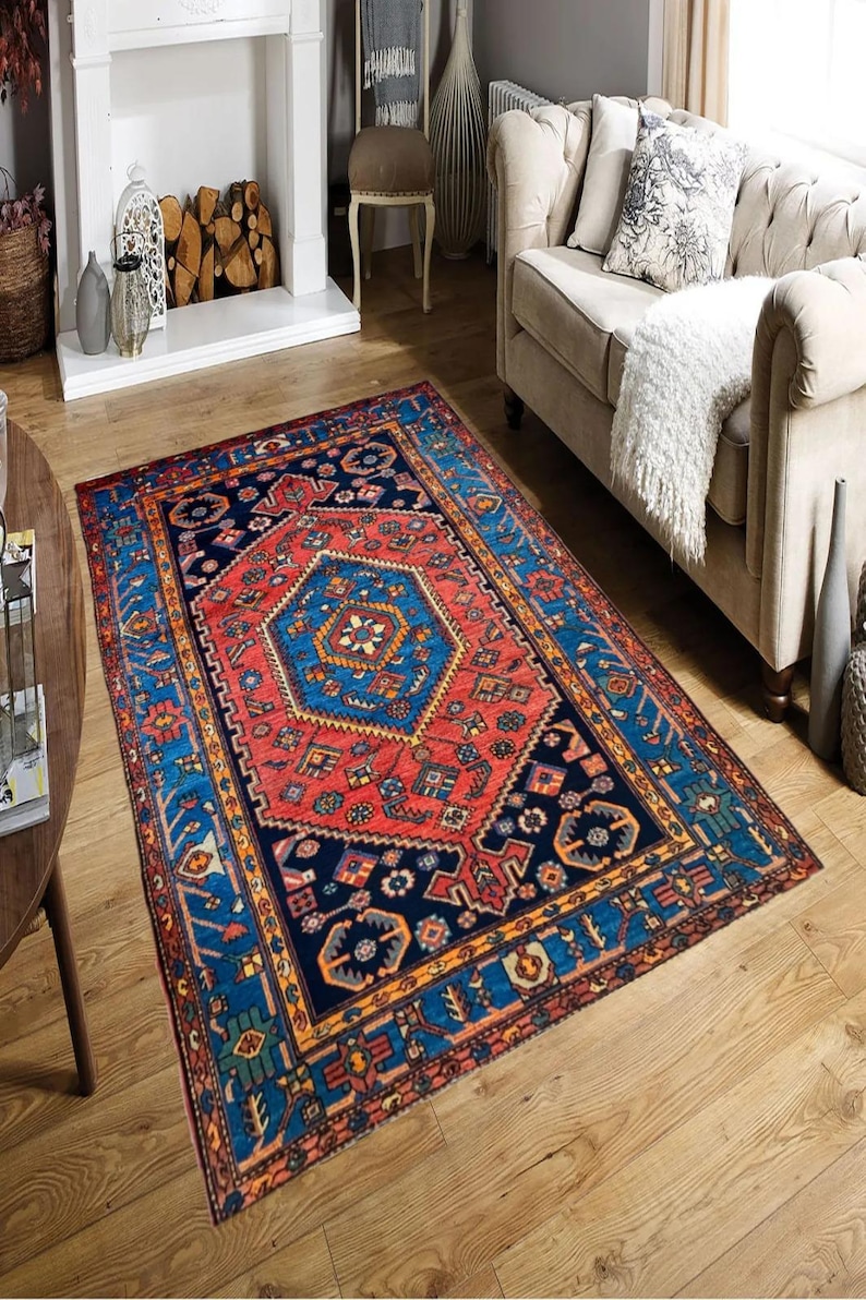 May include: A rectangular area rug with a central geometric design in red, blue, and navy. The rug features a detailed border with repeating patterns and is placed on a hardwood floor. The rug's design includes a central medallion and corner elements.