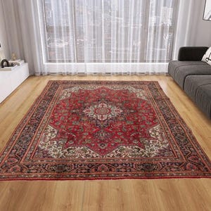 May include: A large, rectangular, red Persian rug with an intricate floral pattern. The rug features a central medallion design and a detailed border in shades of red, cream, and black. It is placed on a hardwood floor.