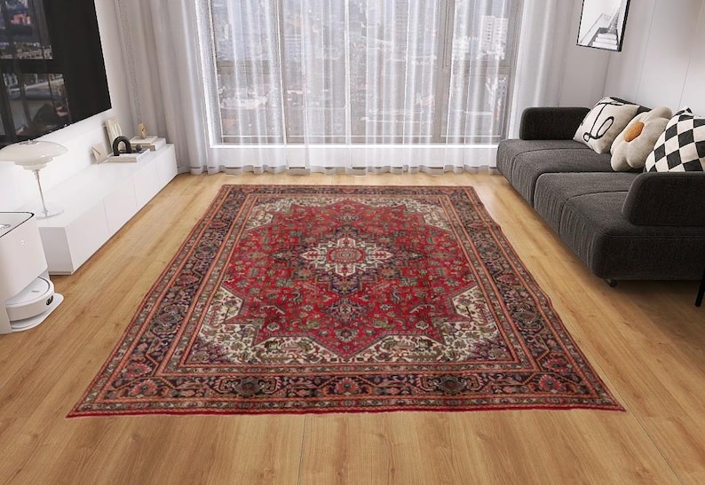 May include: A large, rectangular, red Persian rug with an intricate floral pattern. The rug features a central medallion design and a detailed border in shades of red, cream, and black. It is placed on a hardwood floor.