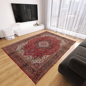 May include: A large, rectangular red Persian rug with an intricate floral pattern dominates a living room. The rug features a central medallion and detailed borders in shades of red, cream, and brown, adding warmth to the space.