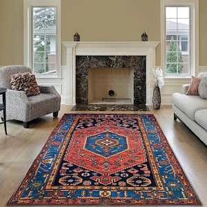 May include: A rectangular, patterned rug with a central geometric design in red and blue. The rug features a navy blue border with intricate patterns and is placed on a hardwood floor in a living room setting.