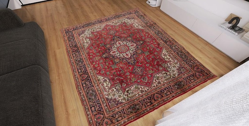 May include: A rectangular red oriental rug with an intricate floral pattern. The rug features a central medallion design with a border of repeating patterns in shades of red, cream, and brown. The rug is placed on a wooden floor.