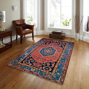 May include: A rectangular area rug with a central geometric design in red and blue. The rug features a navy blue border with intricate patterns and a central medallion. The rug is placed on a hardwood floor in a room with natural light.