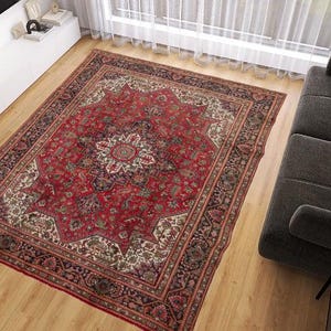 May include: A large, rectangular red oriental rug with a central medallion design and intricate border details. The rug is placed on a hardwood floor in a living room setting, with a dark gray sofa and decorative pillows visible.