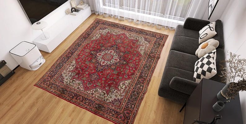May include: A large, rectangular red oriental rug with a central medallion design and intricate border details. The rug is placed on a hardwood floor in a living room setting, with a dark gray sofa and decorative pillows visible.