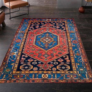May include: A rectangular area rug with a central geometric design in red and blue. The rug features a navy blue border with intricate patterns and a central medallion. The rug is placed on a dark wooden floor.