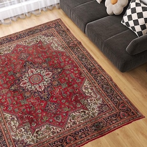 May include: A large, rectangular red Persian rug with an intricate floral pattern and a central medallion. The rug features a border with dark blue and cream accents, and is placed on a hardwood floor.