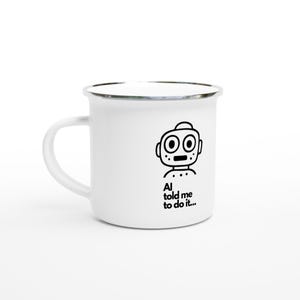 May include: A white enamel mug with a silver rim and a handle on the left side. The front features a black line drawing of a robot head with large circular eyes and the text "AI told me to do it..." printed in a simple black sans-serif font.