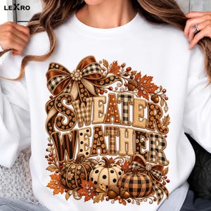 Peut inclure: Un sweat-shirt blanc avec une impression graphique portant le texte "SWEATER WEATHER" dans des motifs à carreaux et à pois marron, noir et beige. Le design comprend des nœuds décoratifs, des feuilles d'automne, des glands et trois citrouilles.