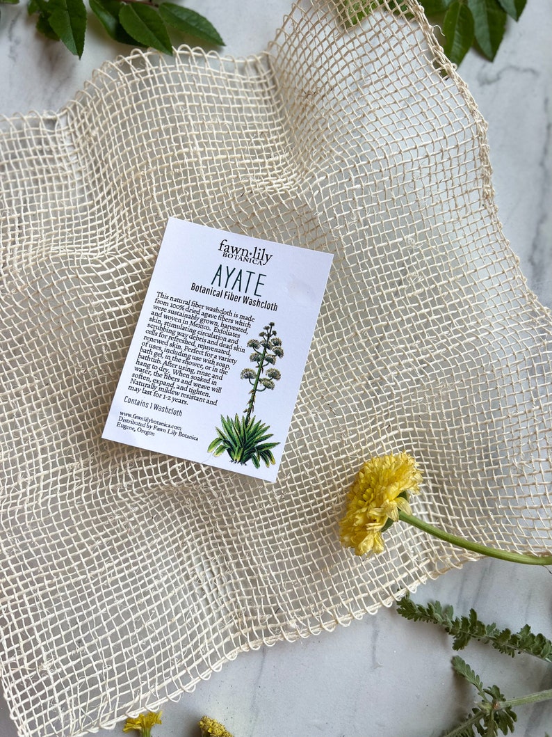 Puede incluir: Un pa&ntilde;o de lavado blanco hecho de fibras de agave, llamado Ayate, se muestra sobre un fondo de fibra natural. El pa&ntilde;o de lavado se fabrica en M&eacute;xico y se cosecha de forma sostenible. El texto de la tarjeta dice "fawn-lily botanica Ayate Botanical Fiber Washcloth".