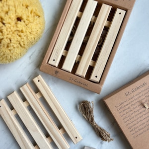 May include: A wooden caddy with a natural sea sponge, a piece of twine, and a toothbrush. The caddy is labeled "Earth Friendly Natural Sea Sponge Caddy" and "St. Gabriel".
