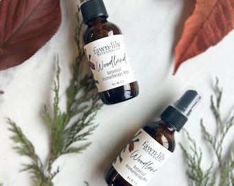 May include: Two brown glass bottles with black spray tops and white labels. The labels read "fawn-lily botanicals Woodland Botanical Aromatherapy Mist Net Wt. 2 fl oz".