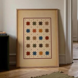 Puede incluir: Una lámina de arte mural rectangular enmarcada que presenta un patrón repetitivo de estrellas de ocho puntas en tonos rojo, azul, amarillo, verde y marrón sobre un fondo crema, encerrado dentro de un borde fino rojo oscuro en un marco de madera clara.