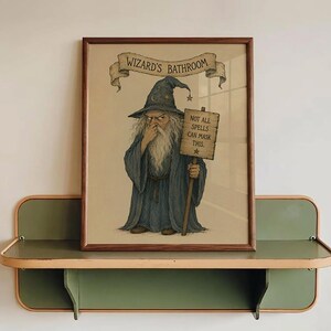 May include: A framed wall art print featuring a wizard in a blue robe and pointed hat holding a wooden sign that reads "NOT ALL SPELLS CAN MASK THIS." Above the wizard, a banner displays the text "WIZARD'S BATHROOM" in black capital letters.