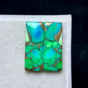 Puede incluir: Dos cabujones de piedras preciosas rectangulares con un mosaico de tonos turquesa, verdes y azules, intercalados con vetas doradas. Las piedras están sobre un fondo blanco, mostrando sus colores vibrantes y patrones únicos.