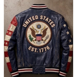 Puede incluir: Chaqueta de cuero azul marino con acabado desgastado. La espalda presenta un gran emblema bordado con las palabras "UNITED STATES" y "EST. 1776". Las mangas tienen detalles en rojo, blanco y azul con estrellas.