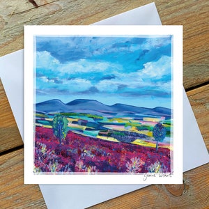 May include: A painting of a landscape with purple wildflowers in the foreground, a forest in the middle ground, and blue mountains in the background. The sky is blue with white clouds. The painting is signed "Jeanne Wishart" in the bottom right corner.