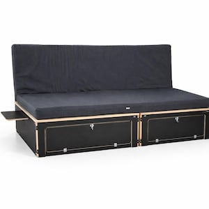 Puede incluir: Un sofá cama negro y de madera natural para furgoneta camper con un cojín y respaldo gris oscuro. El sofá tiene dos compartimentos de almacenamiento con pestillos y una mesa lateral extraíble. El marco es de madera natural.