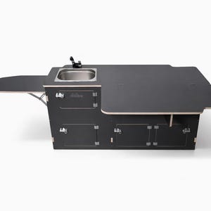 Könnte beinhalten: Dunkelgraue Kücheneinheit für einen Wohnwagen mit Edelstahlspüle, Wasserhahn und mehreren Staufächern. Sie verfügt über eine ausklappbare Arbeitsplatte und eine große Arbeitsfläche. Die Einheit ist für den Außenbereich konzipiert.