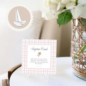May include: A square Scripture card with a pink plaid pattern and the text "Scripture Cards." The card features a quote and an illustration of an angel. A clear plastic card stand is also shown.