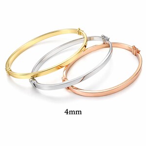 May include: Three 4mm bangles in gold, silver, and rose gold. Each bangle has a simple, smooth design with a clasp closure. The bangles are displayed on a white background.