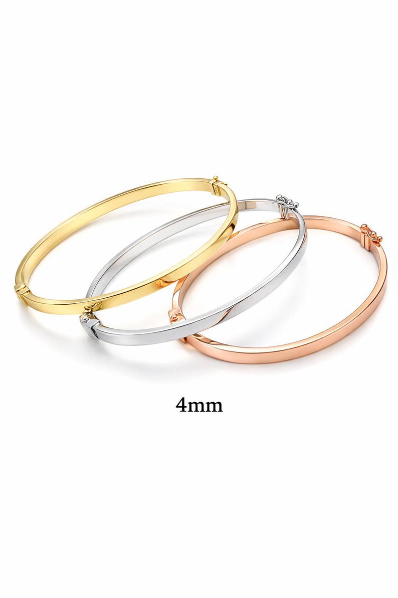 May include: Three 4mm bangles in gold, silver, and rose gold. Each bangle has a simple, smooth design with a clasp closure. The bangles are displayed on a white background.