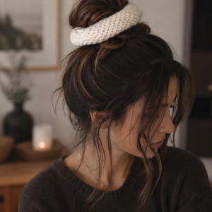 May include: A thick, off-white knitted hair scrunchie with a textured, ribbed surface. The accessory is circular in shape and features a dense, woven yarn construction, providing a soft and voluminous appearance for securing hair in a bun style.