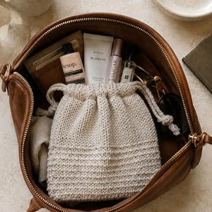 Può includere: Una borsa in pelle marrone contenente una pochette in maglia beige con coulisse, un portacarte color cuoio, un tubetto di crema mani Aesop, una crema mani Byredo Blanche, un prodotto labbra Sugar Rose, un flacone di profumo e occhiali neri.