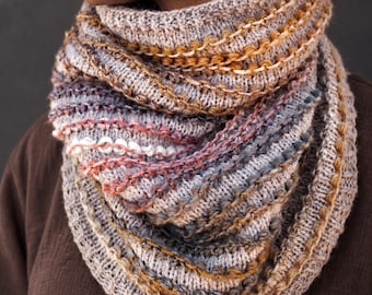 May include: A chunky knit infinity scarf featuring a variegated pattern of beige, grey, mustard yellow, and soft pink yarn. The scarf has a textured, multi-layered appearance with horizontal ribbed sections and interspersed decorative yarn loops.