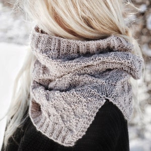 Könnte beinhalten: Eine Frau mit langen blonden Haaren trägt einen grauen gestrickten Schal mit Rollkragen und einen schwarzen Pullover.