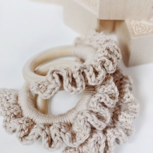 Peut inclure: Un anneau en crochet beige avec un anneau en bois à l'intérieur. L'anneau en crochet a un design à volants.