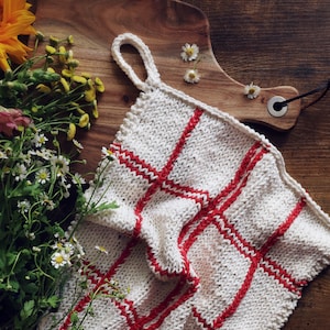 May include: White knitted dishcloth with red stripes, hanging on a wooden cutting board with flowers.