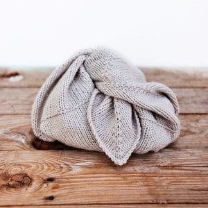 May include: A light gray knitted fabric bunched up on a wooden surface. The fabric is folded into a triangular shape with a pointed tip.