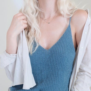 Woman wears a knitted tank top, The Bluebell Camisole knitting pattern, that was knitted in blue yarn. This knit cami top is great for summer and the camisole features a pretty knit texture throughout.
[camisole knit patterns, easy knit patterns]