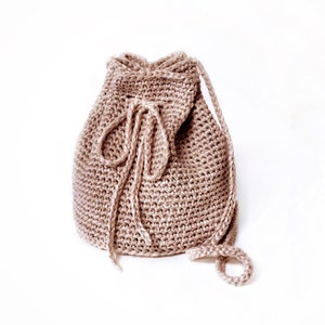 May include: A beige crocheted drawstring bag with a long strap. The bag is made of a soft, textured yarn and has a simple, classic design.